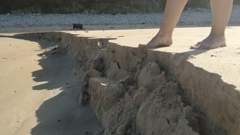 barefoot person steps on sand cliff edge, sand collapses at torimbia beach asturias