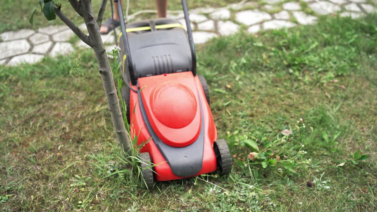 Young boy cutting the grass with a lawn mower in summer time