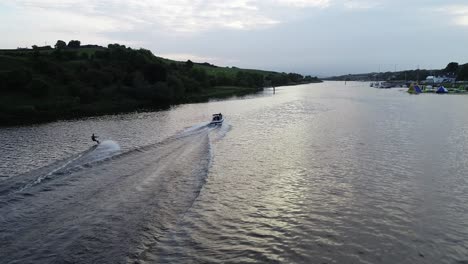 Luftaufnahme,-Person,-Die-Auf-Flusswasser-Ski-Fährt-Und-Schnellboot-Schleppt,-Drohnenaufnahme-Mit-60-Bildern-Pro-Sekunde