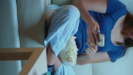 vertical video: woman scrolling on phone eating popcorn