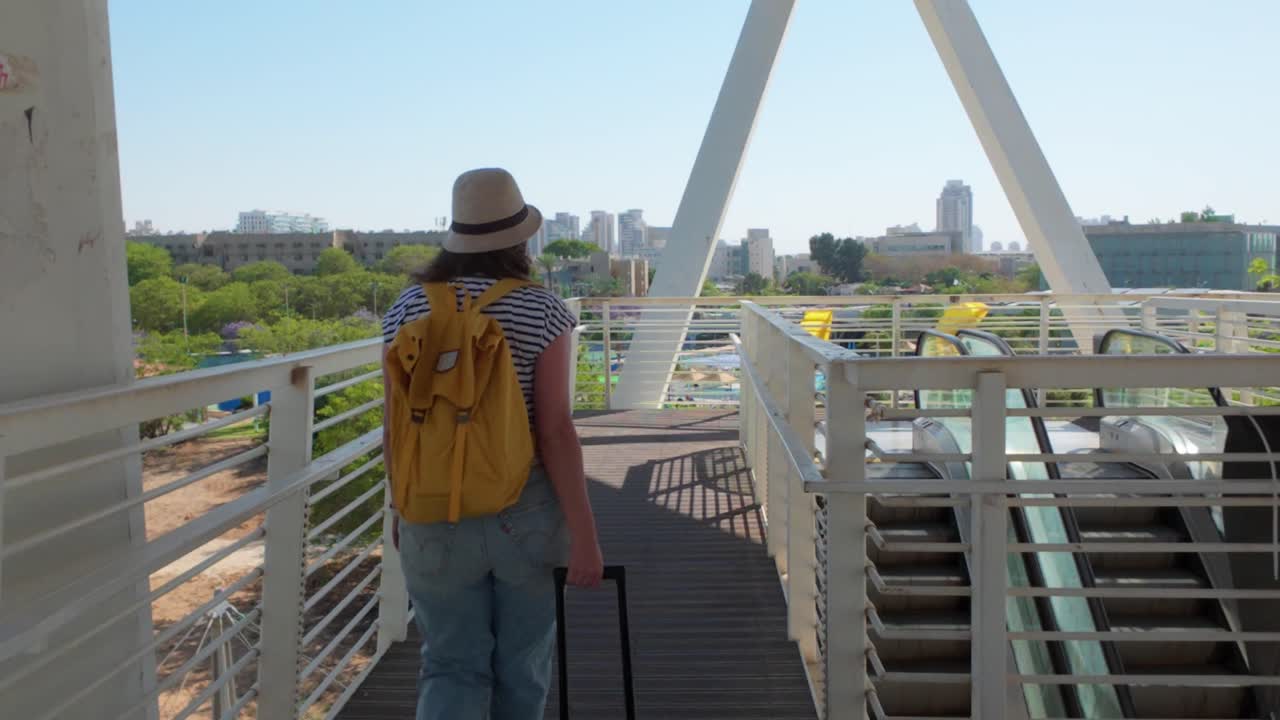 The traveler crosses a pedestrian bridge in the terminal, heading toward her gate.