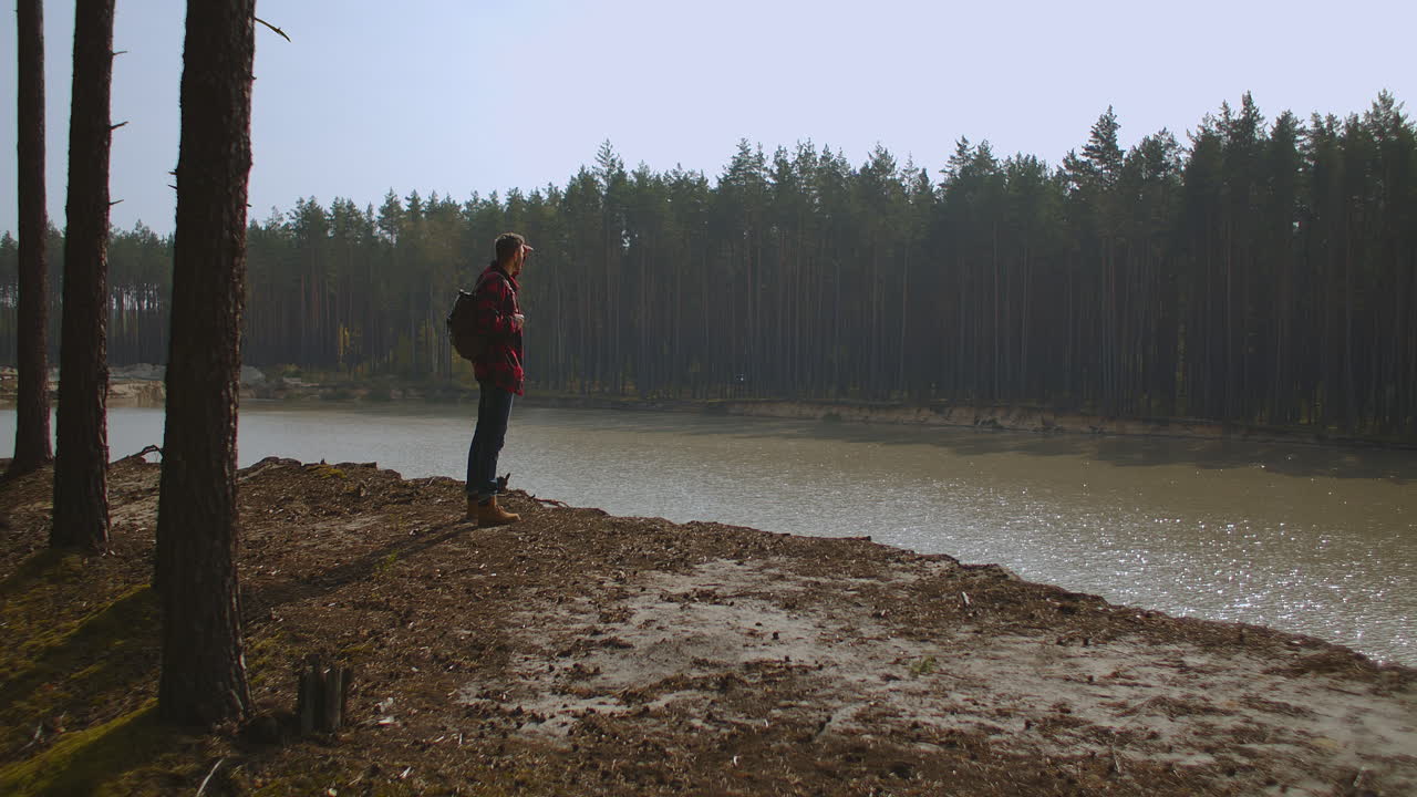 Hiker with a backpack at sunset on the top of a mountain enjoying the sunset with a raised hand in a winner's pose against the background of the river. Travel and vacation concept. High quality 4k footage