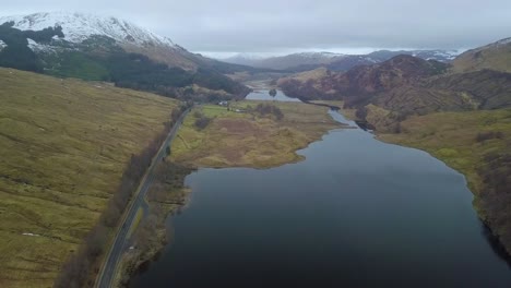 sobrevuelo aéreo fiordo y carretera en las tierras altas de escocia durante el cielo gris y las montañas nevadas en el fondo