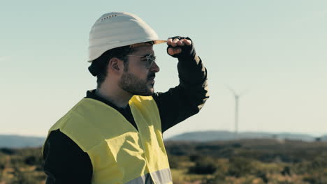 white helmet and reflective vest-clad engineer checks wind turbines in a field of clean energy generators