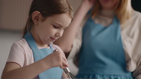 la niña está aprendiendo a cocinar, golpeando huevos o crema en el cuenco en la cocina de casa, infancia feliz