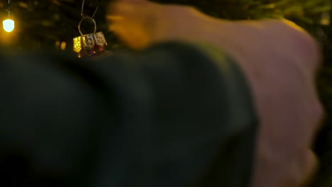 man with green christmas sweater hanging a santa claus ornament in the christmas tree, close up