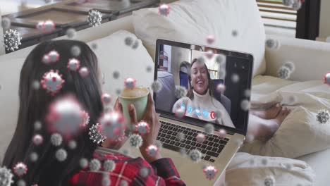 Covid-19-cells-floating-against-woman-having-a-videocall-on-laptop-at-home