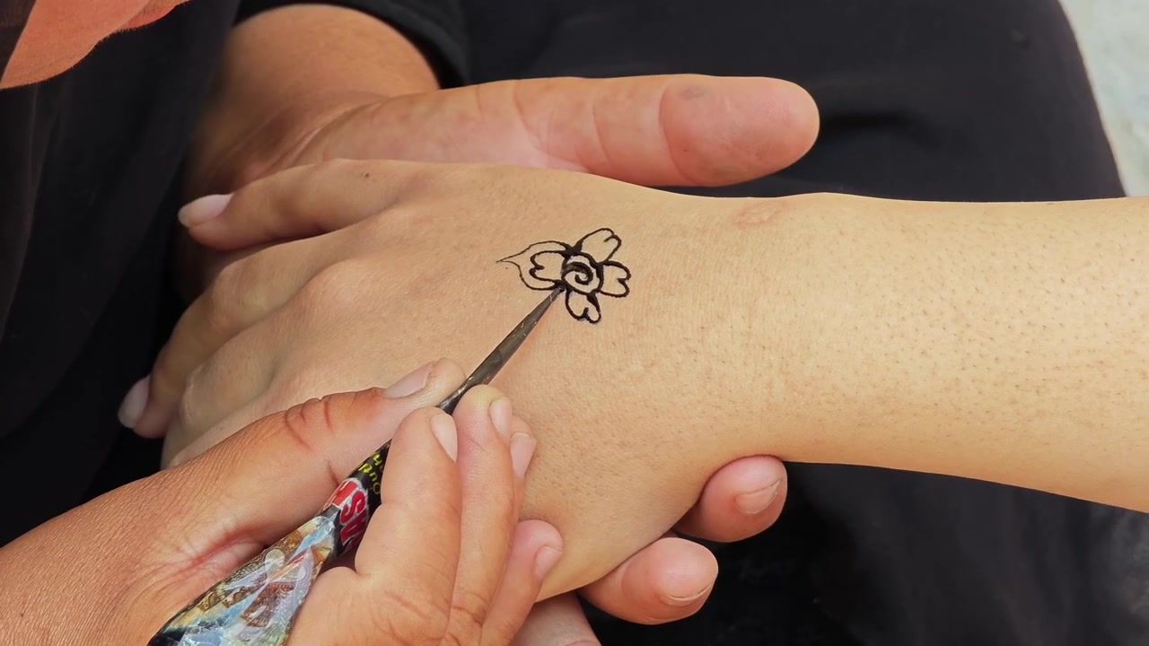 Artista che disegna un delicato tatuaggio all'henné a forma di fiore su una mano