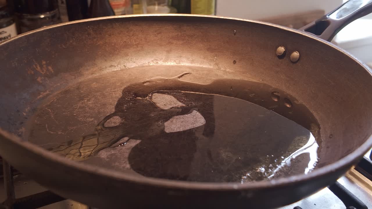 Hot cooking oil sizzling, frying pan on kitchen gas stove hob Close-UP