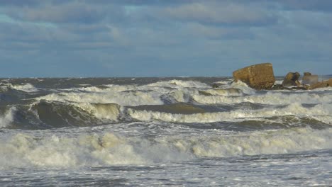 Big-stormy-waves-breaking-against-abandoned-seaside-fortification-building-ruins-at-Karosta-Northern-Forts-in-Liepaja,-slow-motion-wide-shot