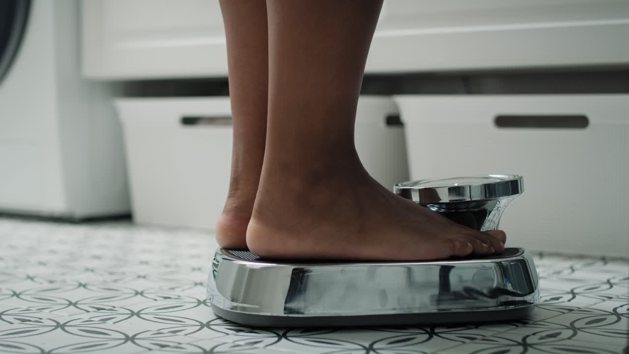 pies de una mujer afroamericana irreconocible pisando la báscula del baño.