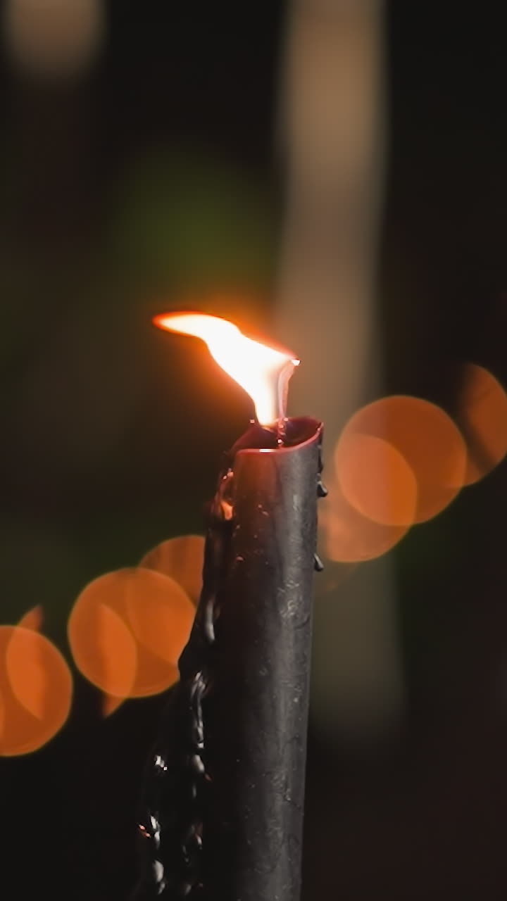 Wavering flame of candle sways gently in breeze. Burning candles perfect for romantic dates stand on table against blurry light garland