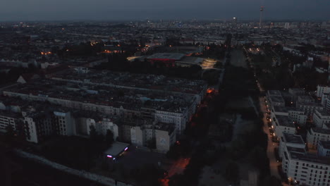 Aerial-view-of-morning-cityscape-with-Fernsehturm-TV-tower.-Fly-above-urban-neighbourhood-modestly-lit-by-street-lights-before-sun-rise.-Berlin,-Germany