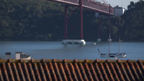 Below-The-Beautiful-Abril-Bridge-In-Portugal-With-A-Boat-Passing-Underneath---Wide-Shot