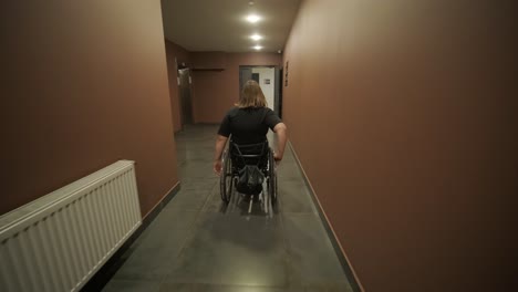 a woman in a wheelchair navigates down a long, dimly lit hallway, symbolizing independence and accessibility in a public or residential building. the scene captures determination and solitude.