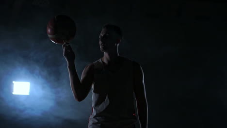 close footage of basketball player spinning ball on his finger, dark misty room with floodlight