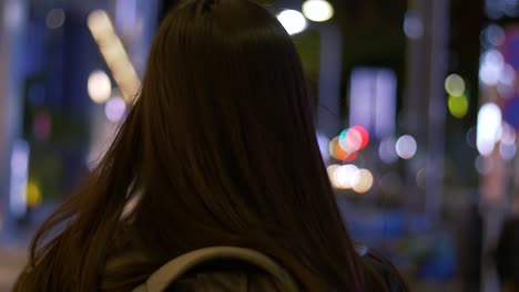 slow motion rear head shot with bokeh of a young, asian female tourist walking around a city at night