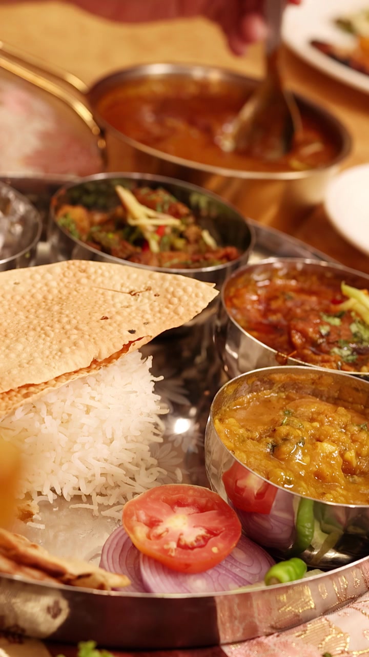 Primer plano de una persona comiendo varios platos indios de una bandeja thali de plata