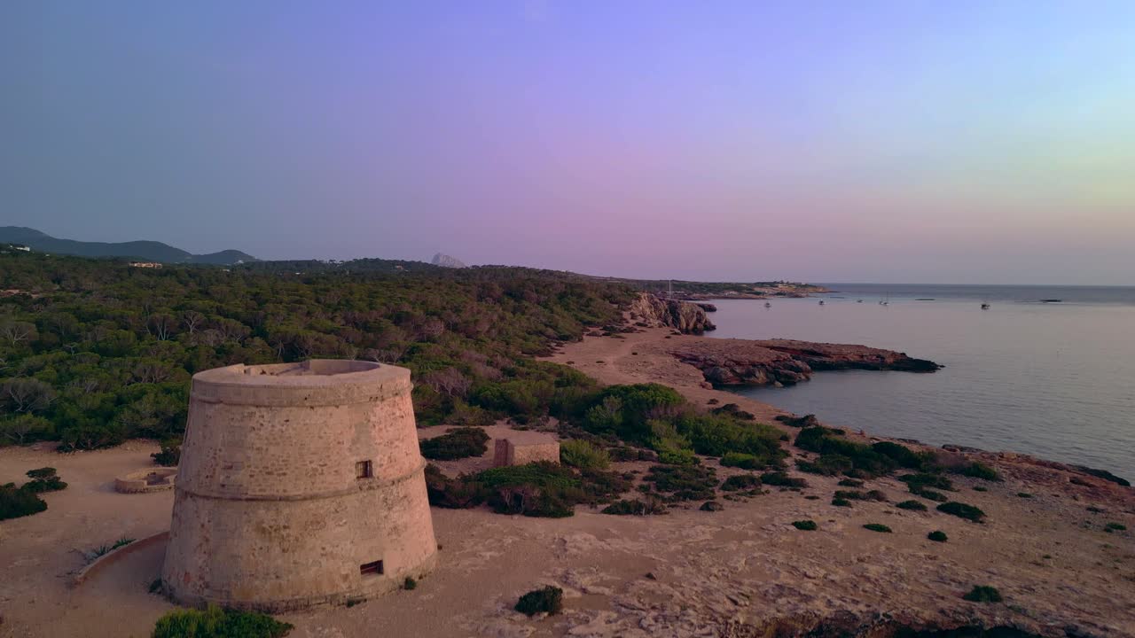 Woman performing yoga poses at sunset near Tower and Es Vedra Island in Ibiza, Spain. Smooth aerial view flight descending drone