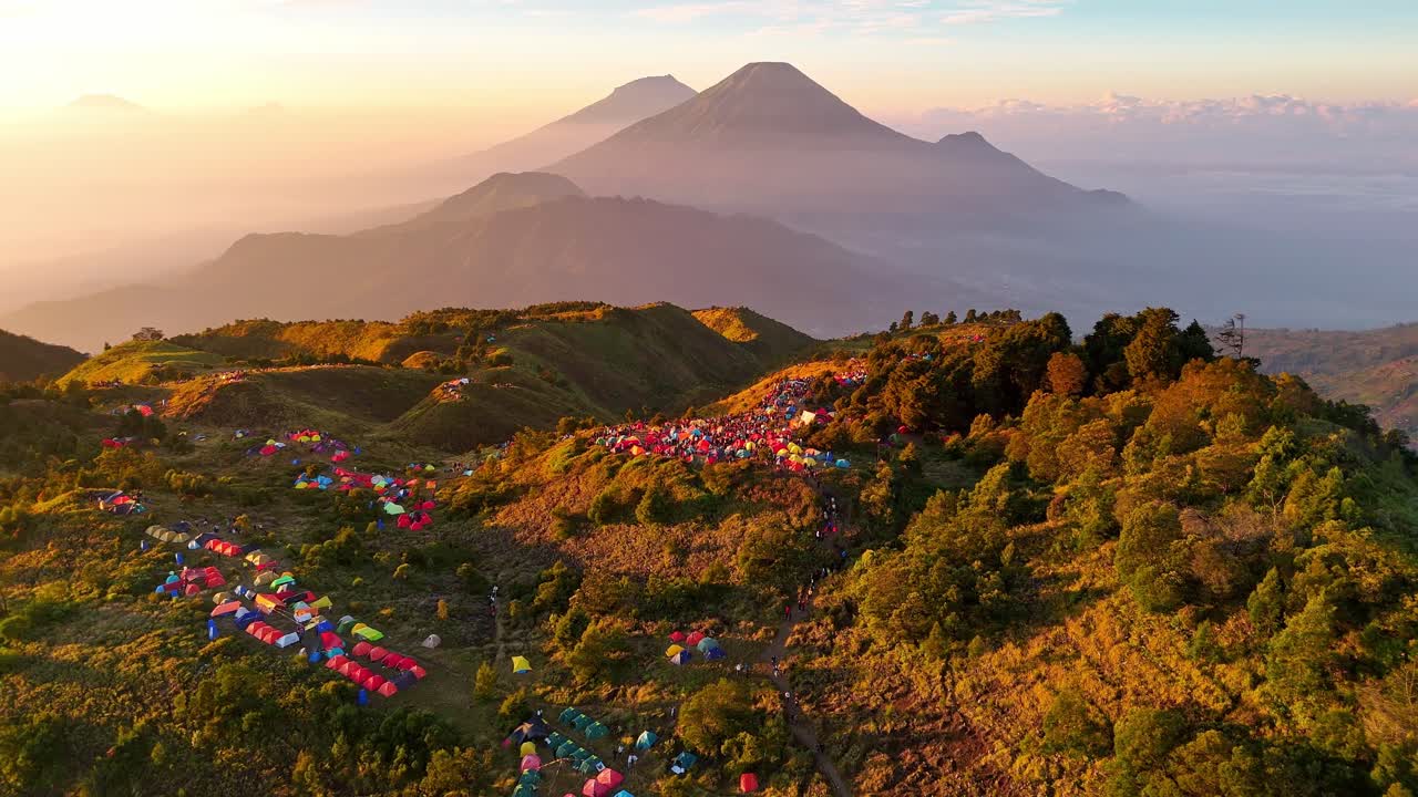 Paesaggio aereo della Cima del Monte Prau. Tende colorate punteggiano la cima erbosa della montagna con un'alba epica e imponenti montagne e dolci colline sullo sfondo.