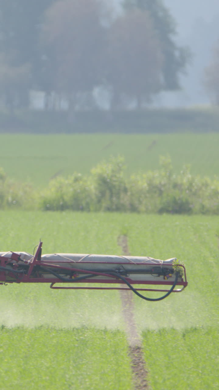 Boom arm of sprayer tractor spray insecticide over crops on farm land. Vertical