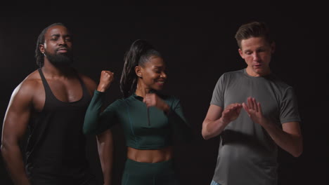 retrato de estudio de atletas sonrientes masculinos y femeninos en ropa de fitness divirtiéndose posando y flexionando los músculos contra un fondo negro