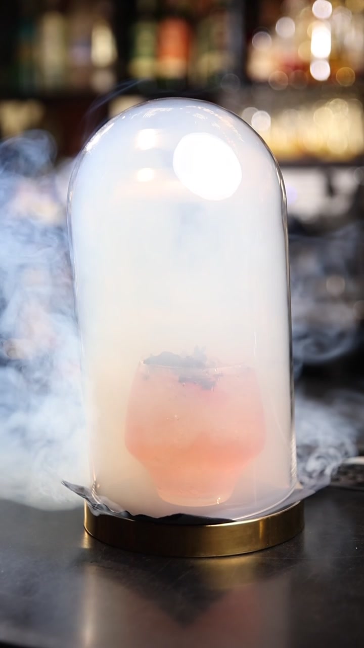 Élégant cocktail rose infusé de fumée sous une cloche en verre