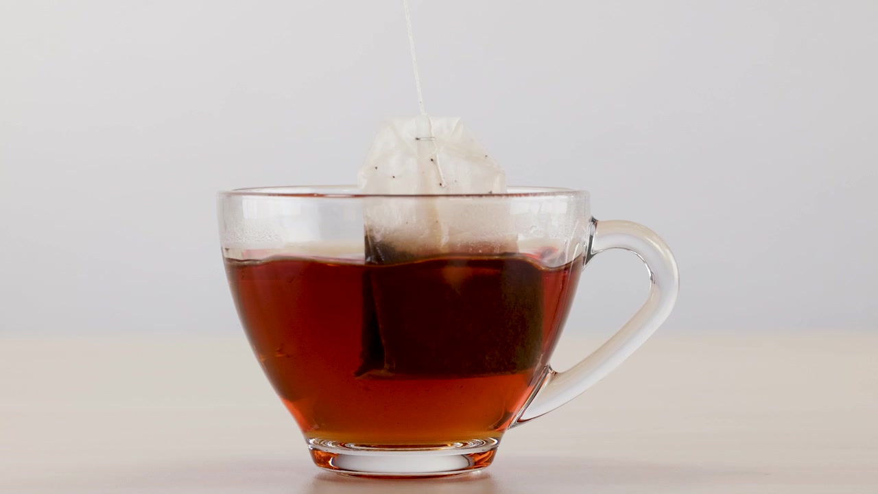 Primo piano di una bustina di tè in infusione in acqua calda all'interno di una tazza di vetro trasparente