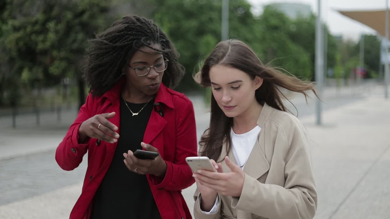 Two women walking along street, one swiping pictures on phone