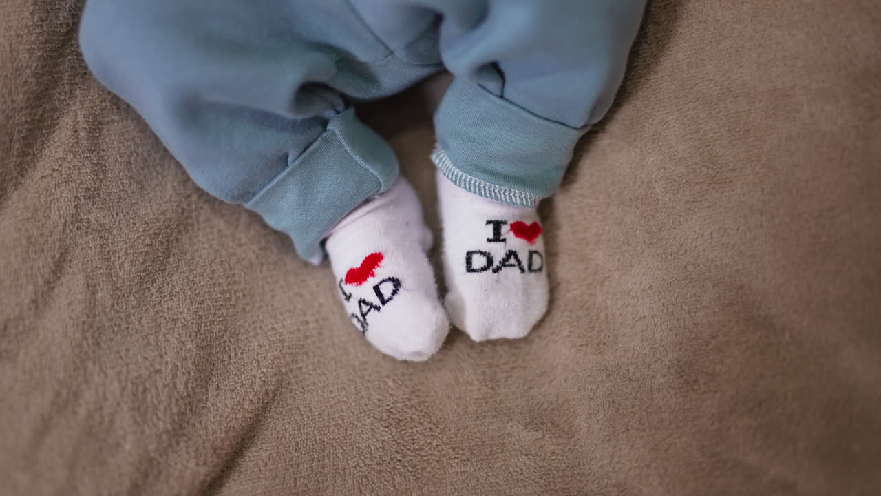 Adorable babe's feet in tiny socks. I love you dad socks on the little feet on the grey backdrop. Close up.