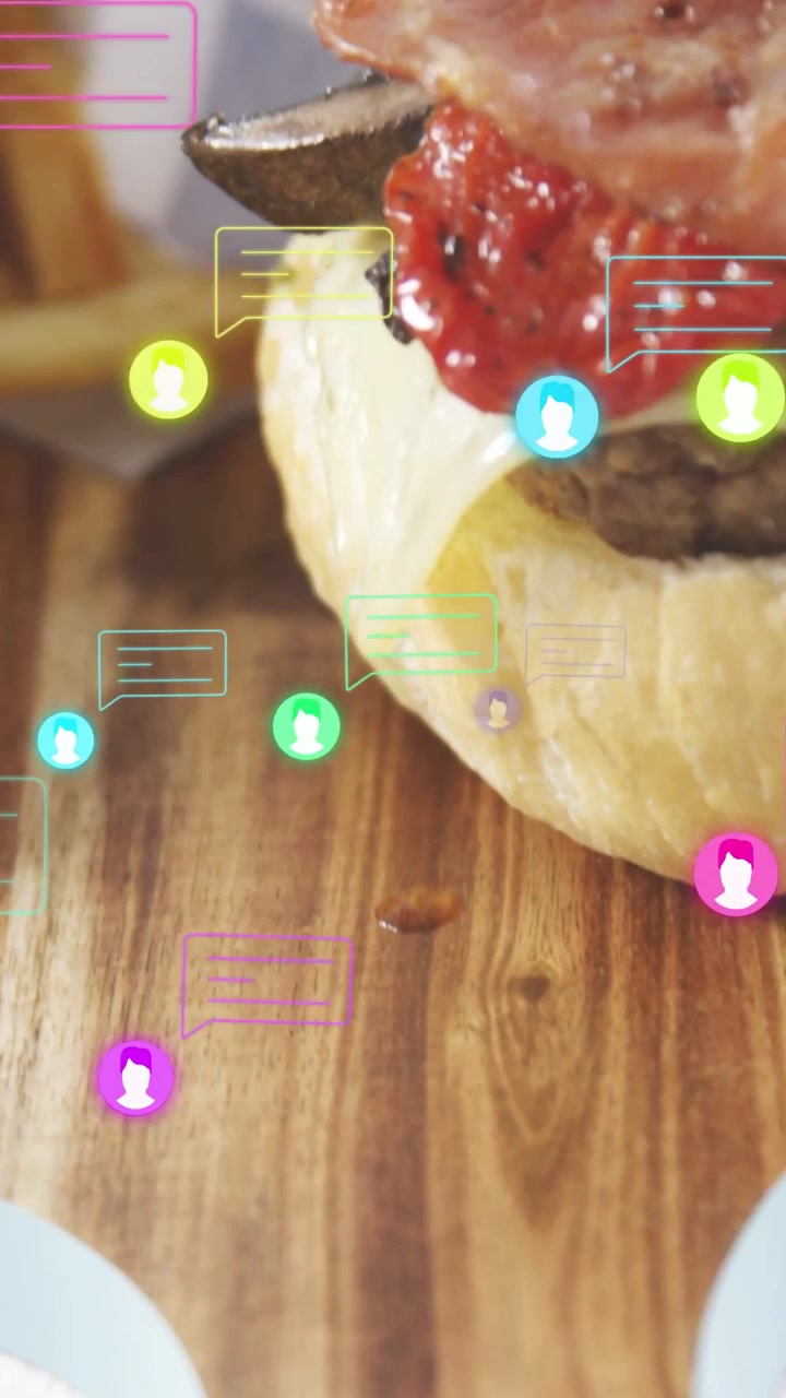 Video vertical: Pan superior cayendo para iniciar el montaje de una hamburguesa, mientras unas pinzas colocan tocino en una tabla para promoción.