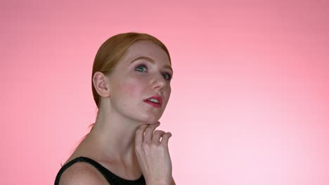 A-close-up-of-a-woman-framing-her-face-with-her-hand,-looking-into-the-camera-with-her-mouth-slightly-open,-on-a-seamless-studio-background