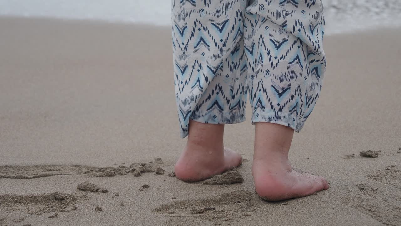 Persons fötter står på sandstrand när havsvågor sköljer in