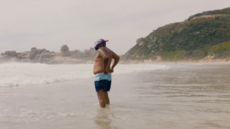 Lustiger-Afroamerikanischer-Mann,-Der-Mit-Flossen-Am-Strand-Im-Meerwasser-Spaziert-Und-Sich-Zum-Schwimmen-Bereit-Macht,-Um-Den-Sommer-Am-Meer-Zu-Genießen,-4k