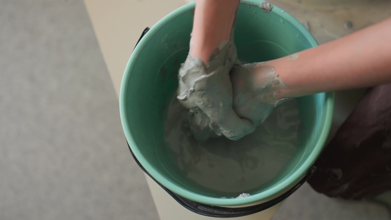 Hands shape clay. Energetic hands sculpt and wash moist clay. Hands vigorously mold and cleanse damp clay during art session. Creative hands actively sculpt and wash wet clay in studio environment