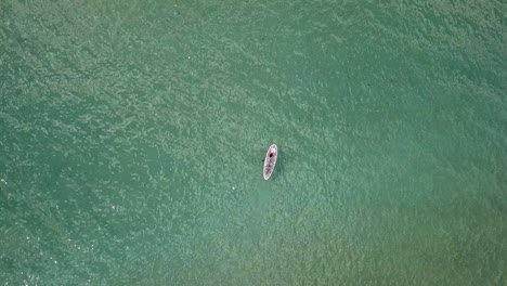 vista de arriba hacia abajo de una mujer arrodillada en un sup y remando alrededor de las aguas del mar egeo