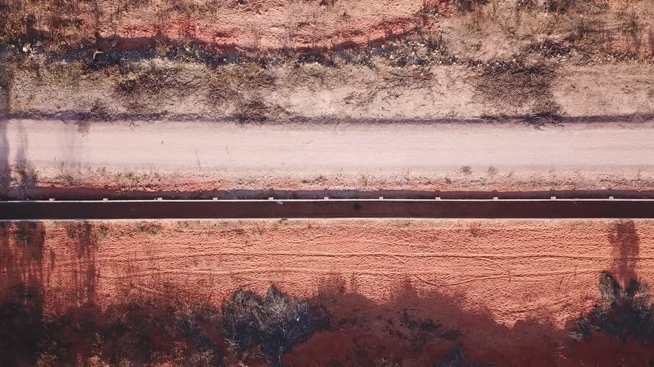 top view of a motorbike driving trough a deserted red sand road casting a shadow from the left side to the right