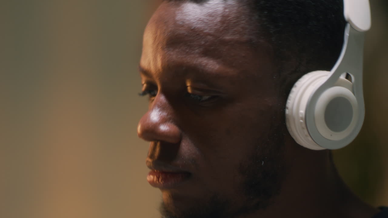 African American Drummer Listening to Music Black Man Listening to Music in Wireless Headphones and Playing Drums in Dim Studio in Evening at Home