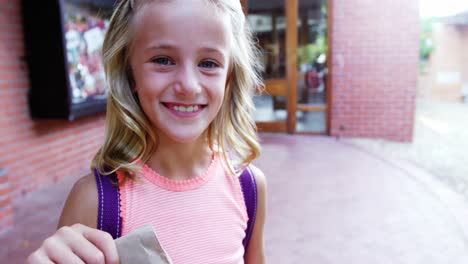 Portrait-of-happy-schoolgirl-holding-paper-bag-in-campus-at-school