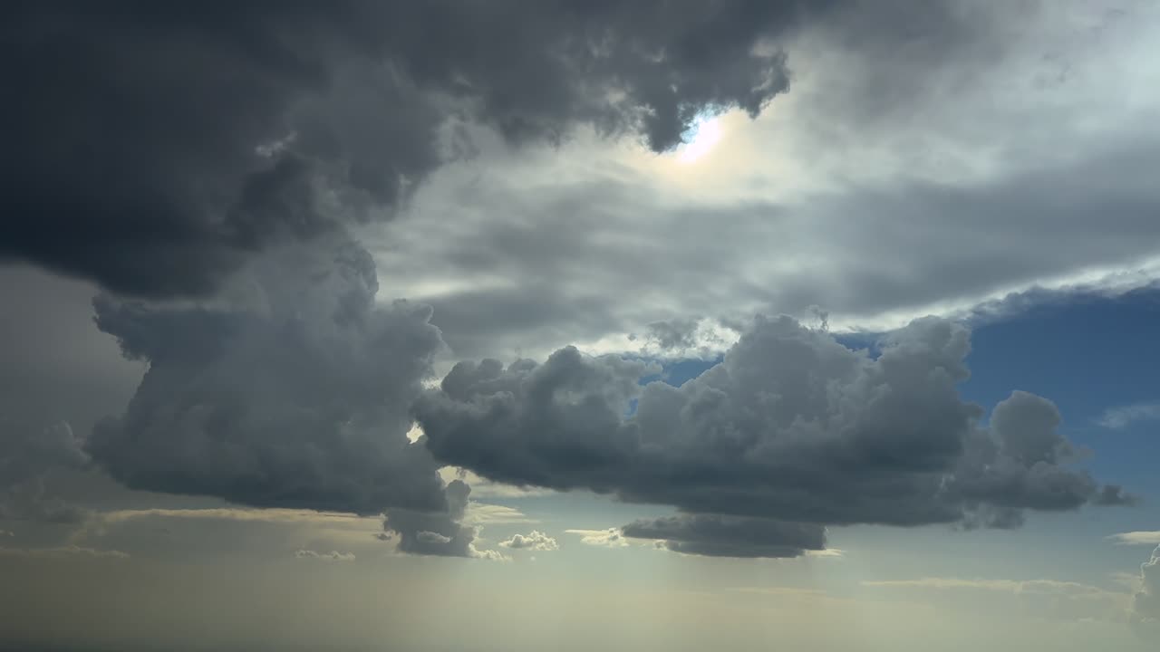 An aerial cloudscape recorded from a jet cockpit while flying through a stormy sky full of threatening storm clouds under a blue sky with a radiant sun above
