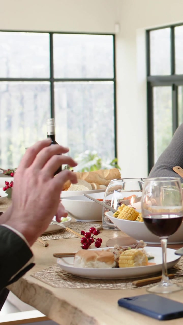 Vertical video: Talking left diner in green top gesturing grabbing fork reaching glass at home meal