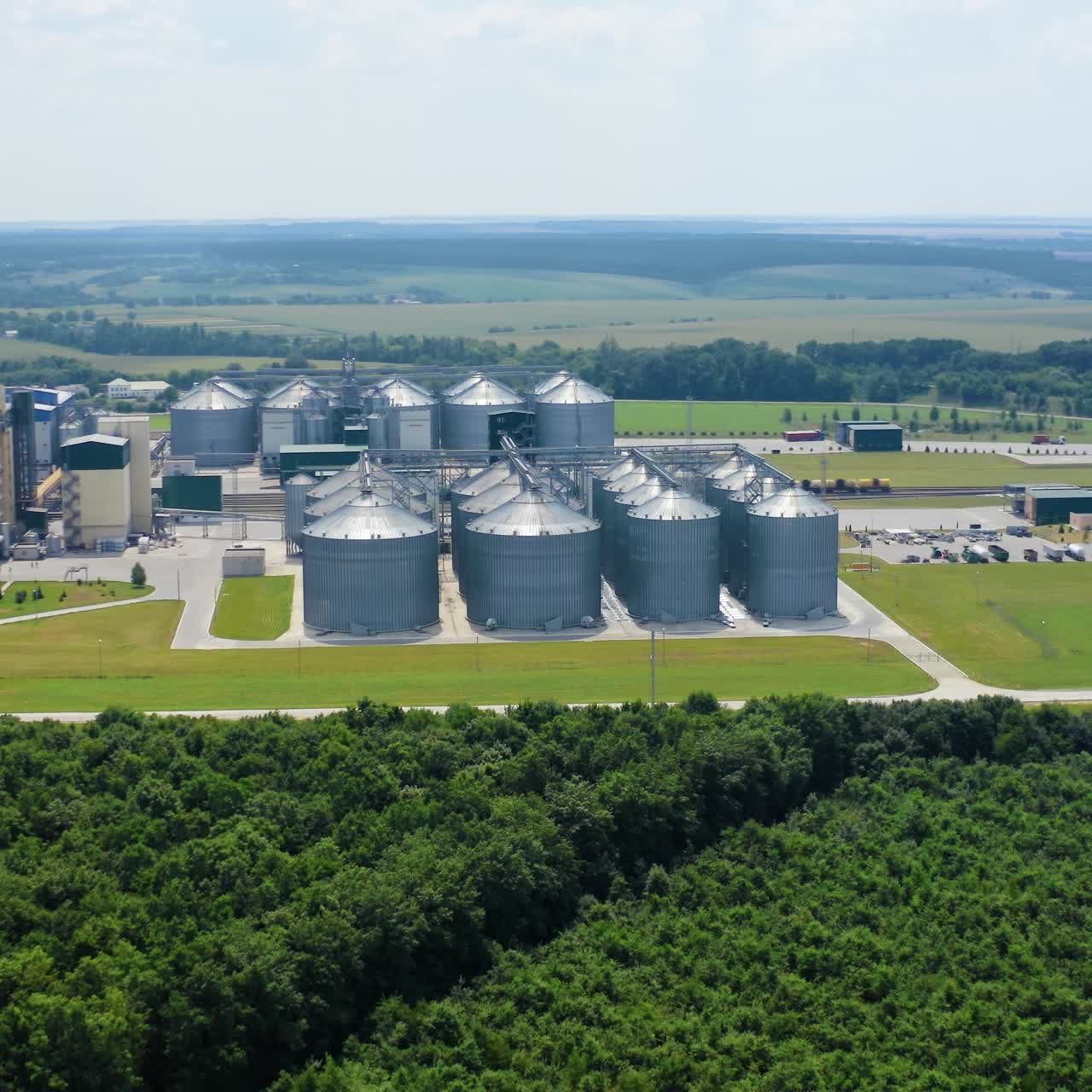 Modern silos on field. Industrial zone for grain storage among green nature. Warehouse for agribusiness in the countryside. Aerial view