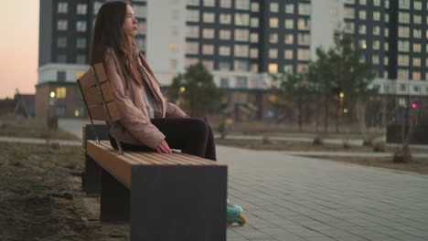 a girl in a peach jacket and black trousers is seen rollerblading towards a park bench. the image captures the moment before she sits down to rest, with her rollerblades visible on the paved path