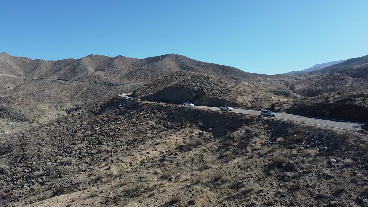 línea de vehículos que circulan por una carretera desértica en un paisaje montañoso, vista aérea de drones