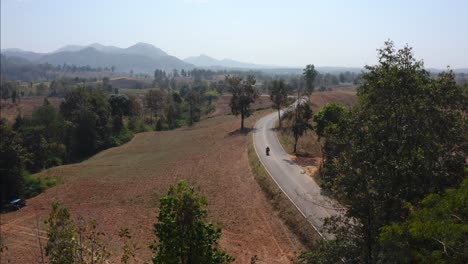 tracking shot of biker riding motorcycle on calm rural road, mae hong loop, thailand