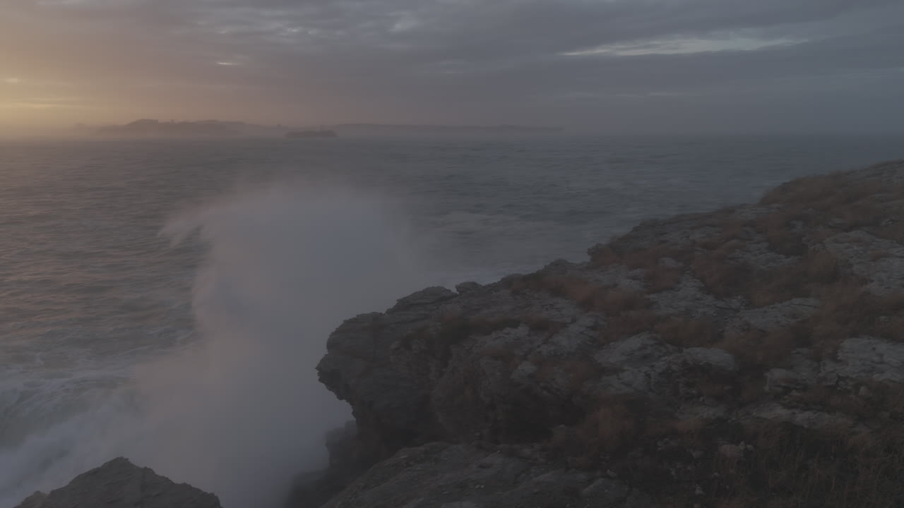 Mohutné oceánské vlny tříštící se o skalnaté útesy při západu slunce.