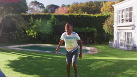 african american dad and son playing with football together in the garden on a bright sunny day