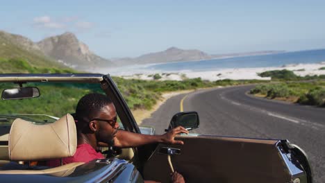 african american man wearing sunglasses stepping out of convertible car on road