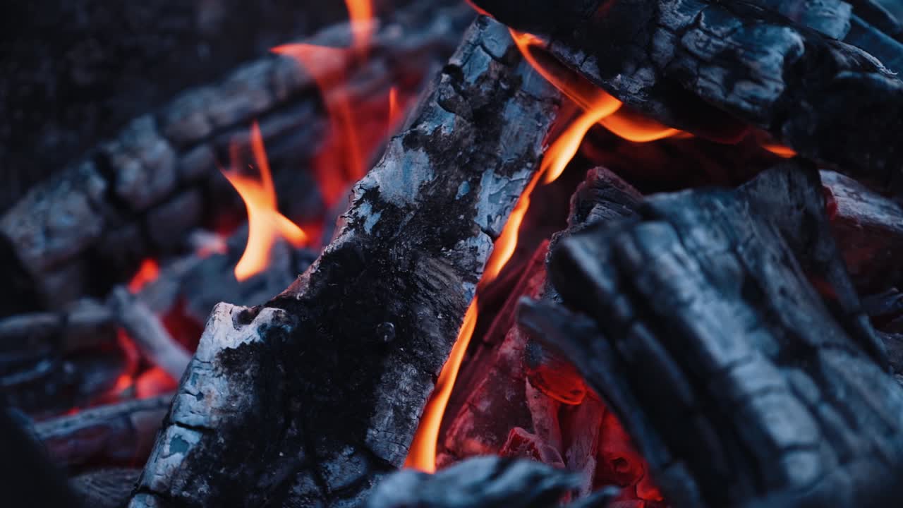 Smoldered logs in burnt fire. Dark firewood with light flame in slow motion. Close-up.