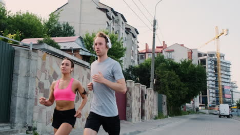 Schönes-Läufermädchen-Mit-Airpods-Und-Sportlicher-Junger-Mann-Mit-Kopfhörern,-Die-Zusammen-In-Der-Stadt-Laufen